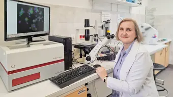 kobieta ubrana w fartuch siedzi przy mikroskopie w laboratorium 